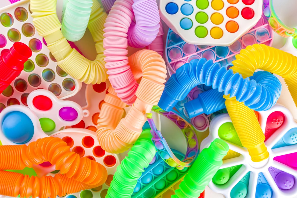 A flat-lay set of bright fidget toys including squishies, pop-its and pop tubes