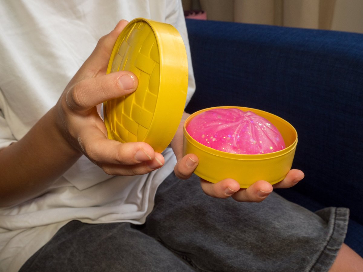 Child's hands unboxing a cute pink glittery squishy dumpling toy from a yellow steamer basket