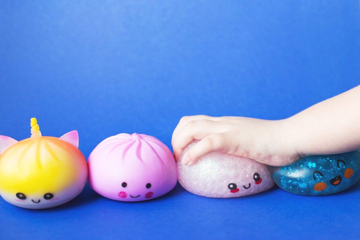 A child's hand squeezing a cute squishy toy against a bright blue background